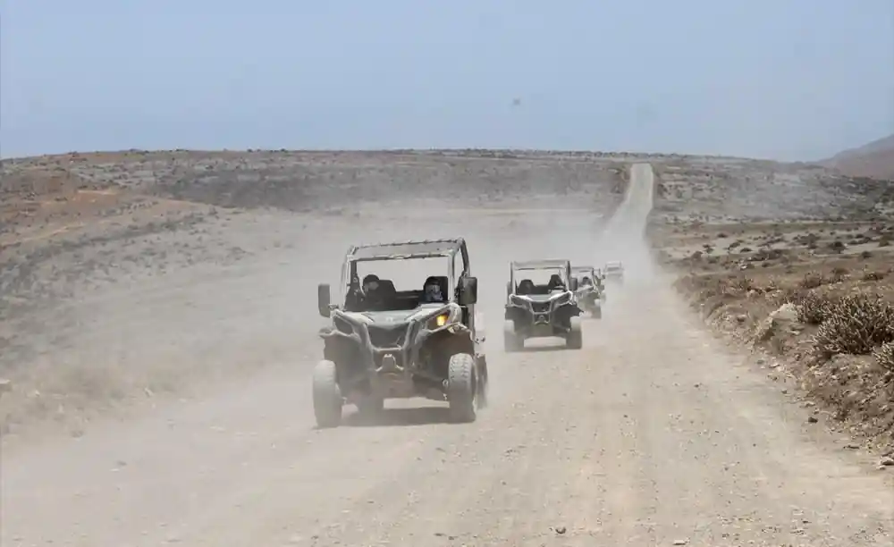 Buggies driving on unpaved dusty track through sparse scrubland