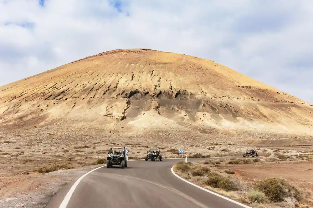 Buggies on paved road approaching distinctive cone volcano
