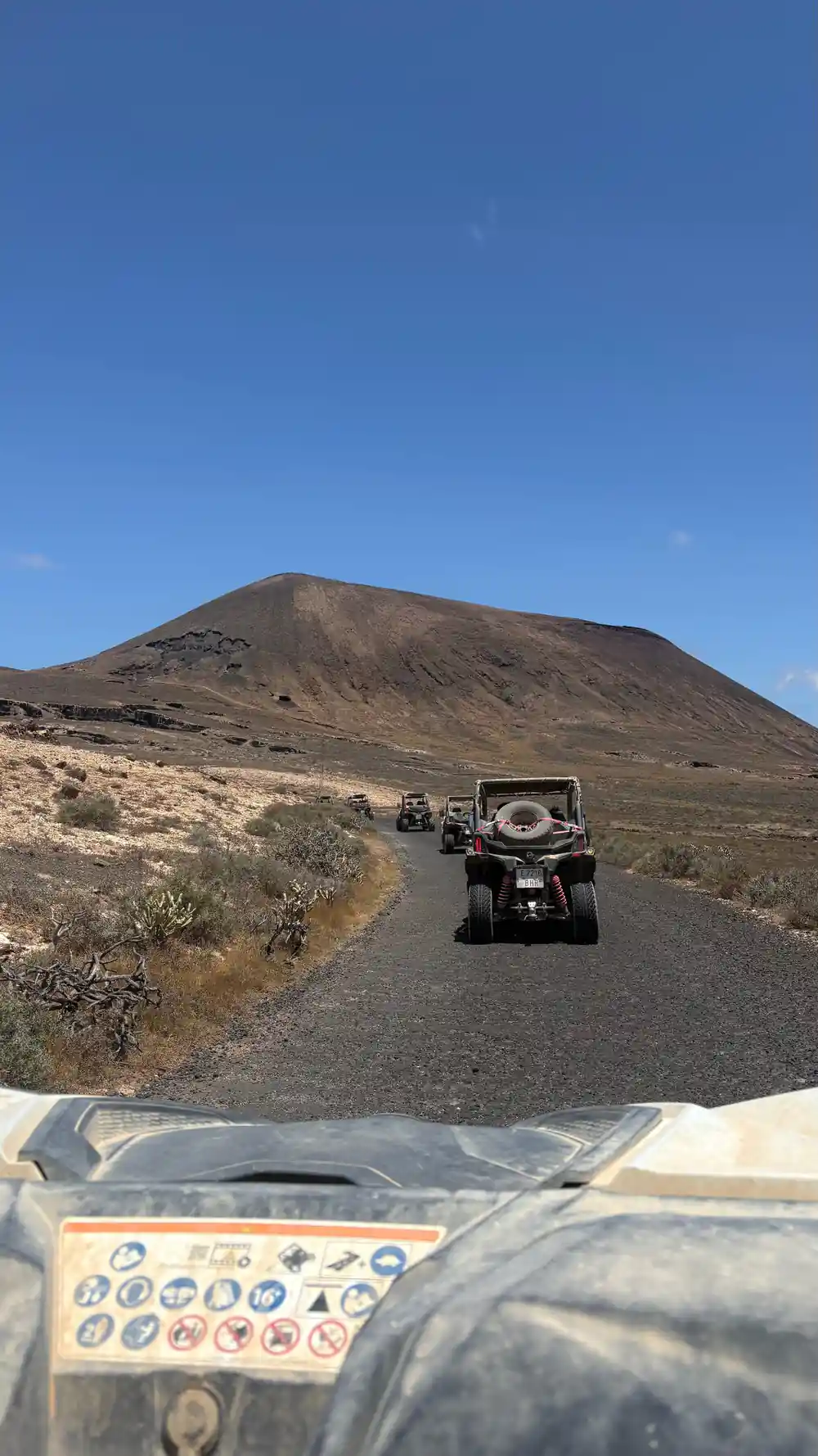 Buggy driving on black road with dark volcanic cone ahead