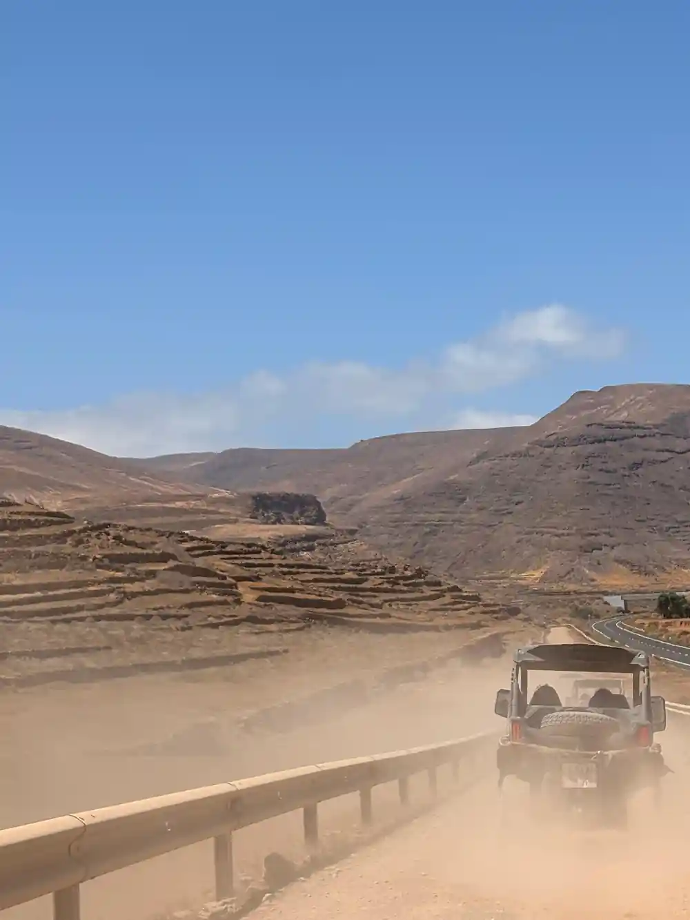 Buggy vehicle driving on dusty desert road with mountains