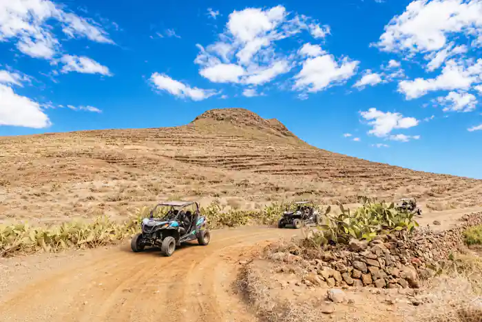 Buggy vehicles on dirt road with volcanic mountain backdrop