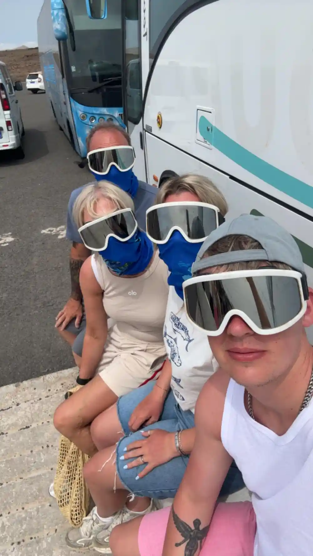 Four people wearing ski goggles outside tour buses