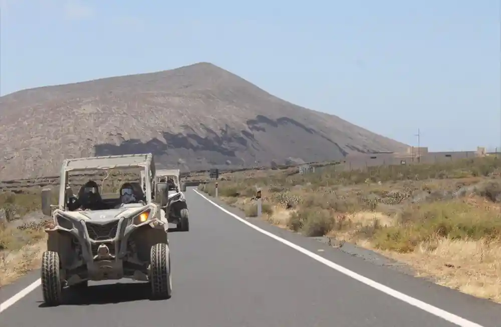 Multiple buggies on paved road through arid volcanic landscape