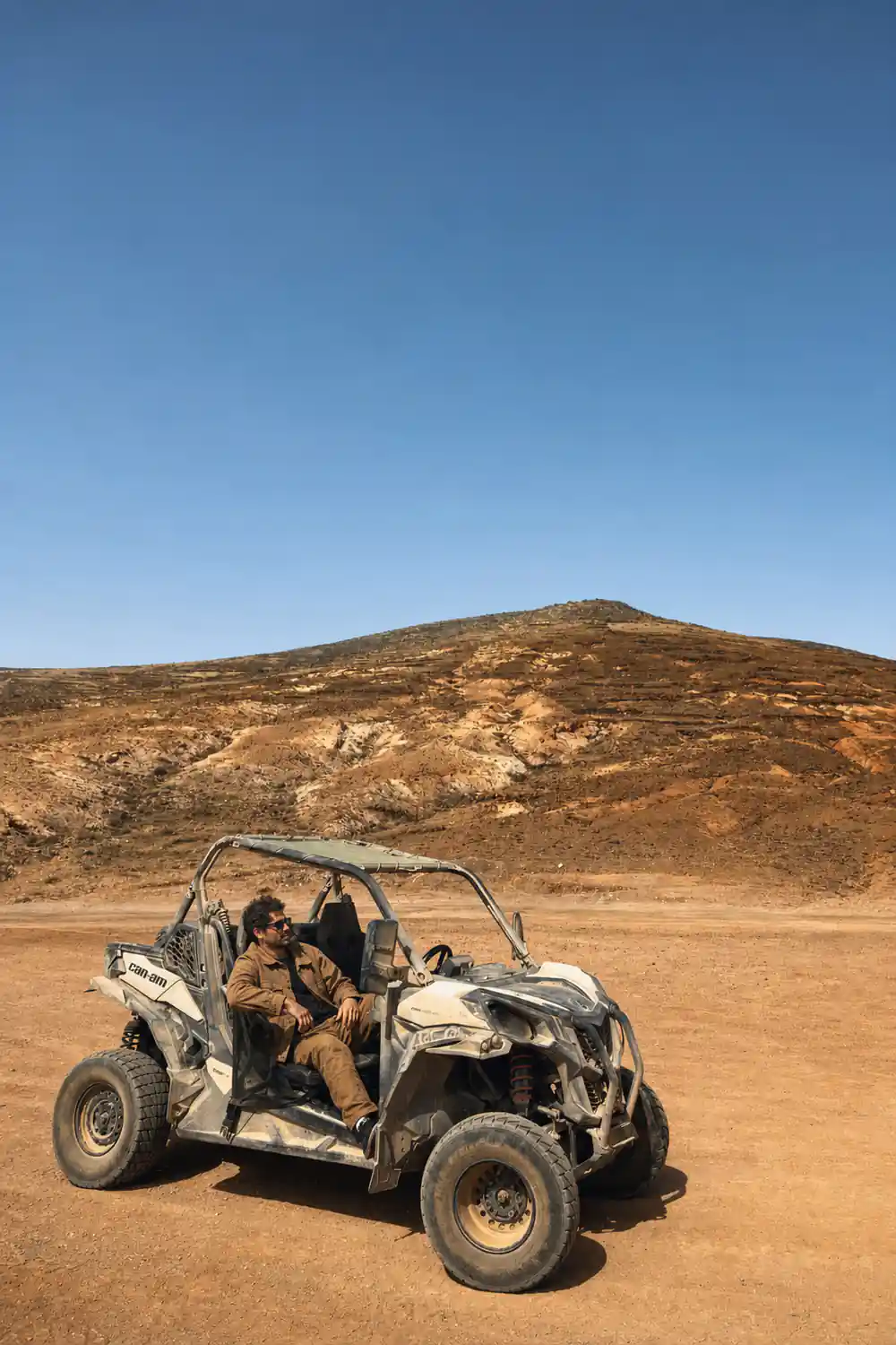 Single white buggy parked on red sand with brown hill backdrop