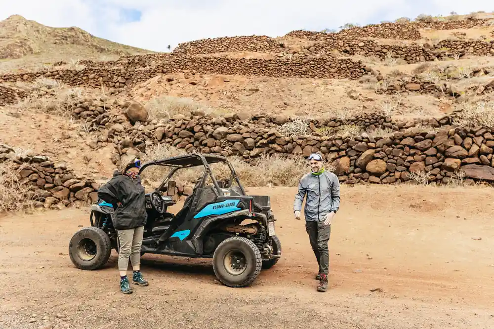 Two people standing next to blue buggy in rocky terrain