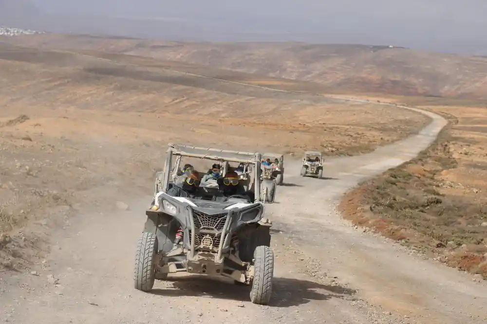 White buggy driving on dusty desert road with others following